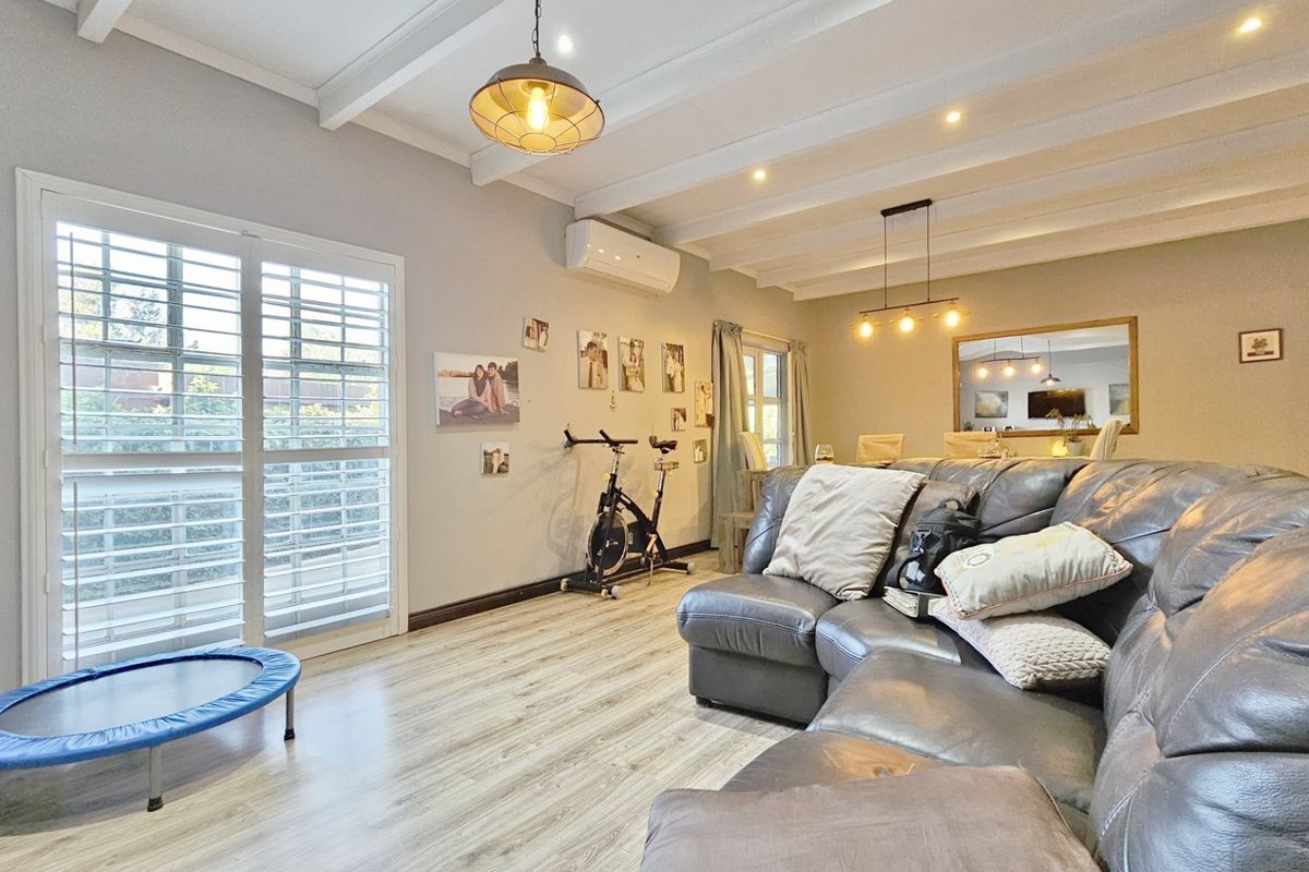 Spacious living room featuring exposed beam ceilings, laminate flooring, split system air conditioning, and sliding glass doors with plantation shutters.