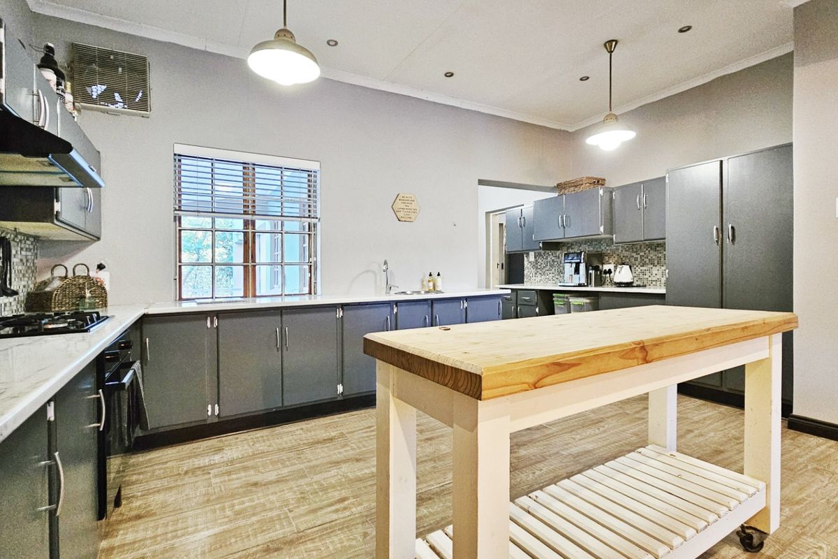 A well-maintained kitchen featuring grey cabinetry, a gas hob, mosaic tile backsplash, and wood-look laminate flooring with a central prep island.