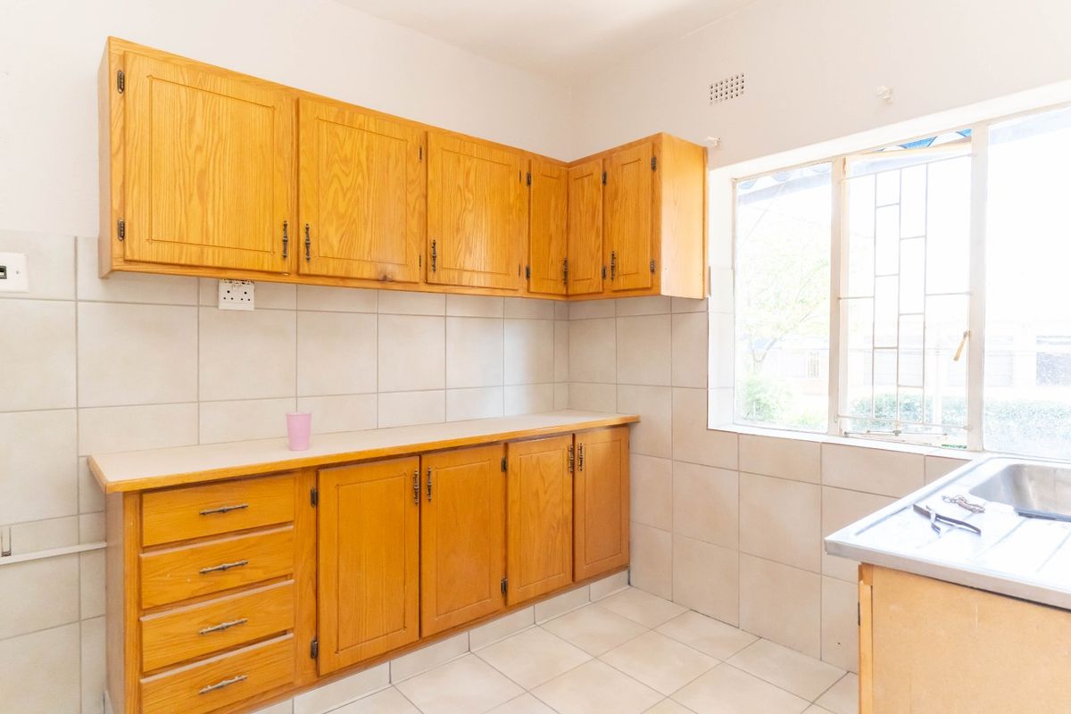 A functional kitchen featuring wooden cabinetry, tiled backsplash, tiled flooring, and a stainless steel sink, offering a clean and practical workspace.