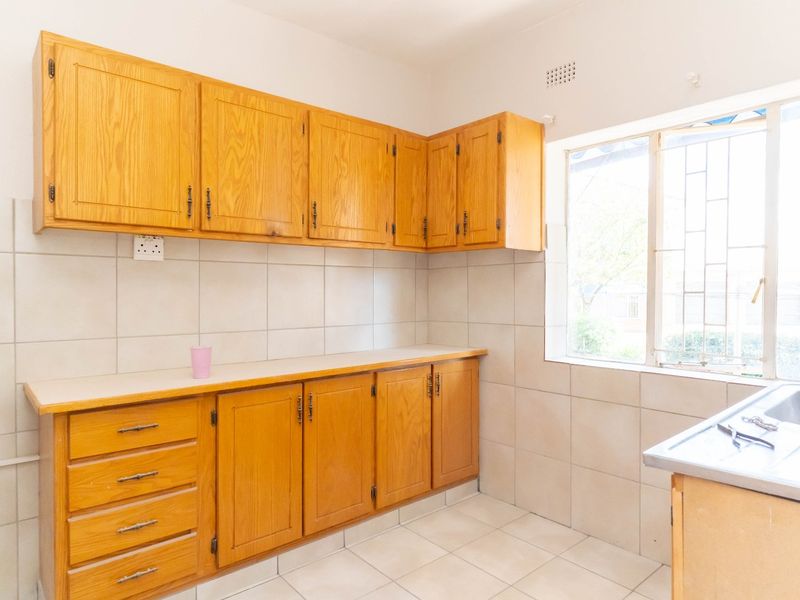 A functional kitchen featuring wooden cabinetry, tiled backsplash, tiled flooring, and a stainless steel sink, offering a clean and practical workspace.