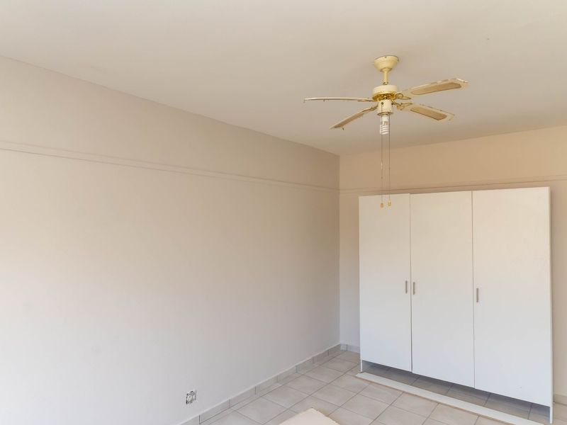 A simple, empty bedroom featuring tiled flooring, a ceiling fan, and a built-in white wardrobe.