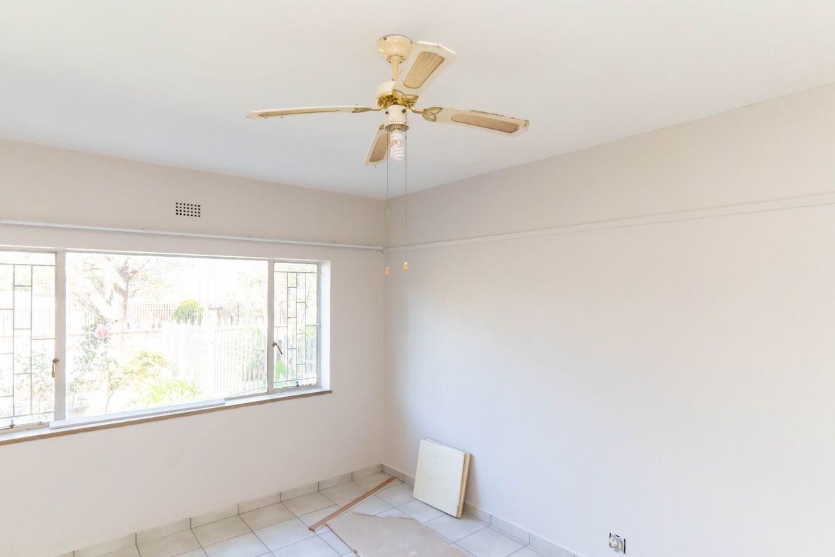 An empty bedroom featuring tiled flooring, a large window for natural light, and a ceiling fan.