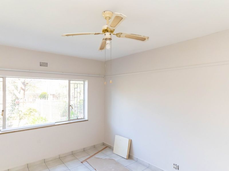 An empty bedroom featuring tiled flooring, a large window for natural light, and a ceiling fan.