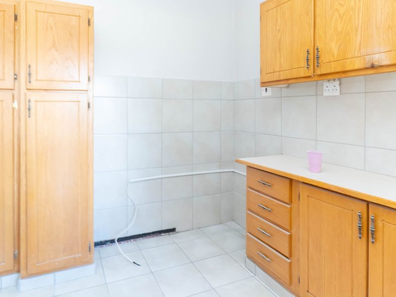 A dated kitchen area featuring wooden cabinetry, tiled backsplash, and tiled flooring, currently vacant and requiring minor repairs to exposed wiring and trim.