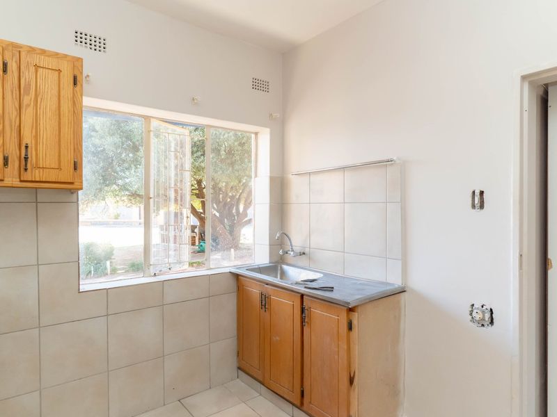A compact, empty kitchen featuring wooden cabinetry, a stainless steel sink, and tiled splashbacks, requiring minor electrical repairs and cosmetic updates.