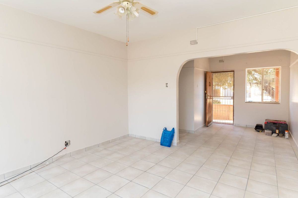An open-plan living area featuring neutral tiled flooring, a ceiling fan, and an arched entryway leading to the front door.