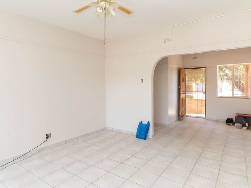 An open-plan living area featuring neutral tiled flooring, a ceiling fan, and an arched entryway leading to the front door.