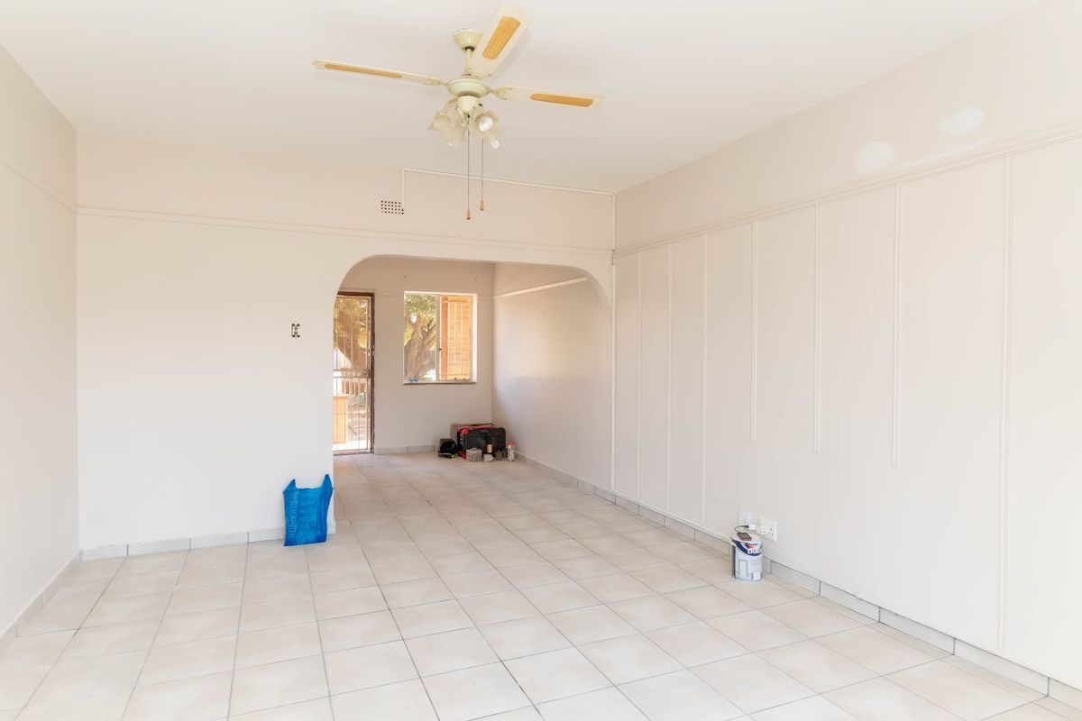 An empty living room featuring tiled flooring, a ceiling fan, and decorative wall paneling, currently undergoing minor wall repairs.