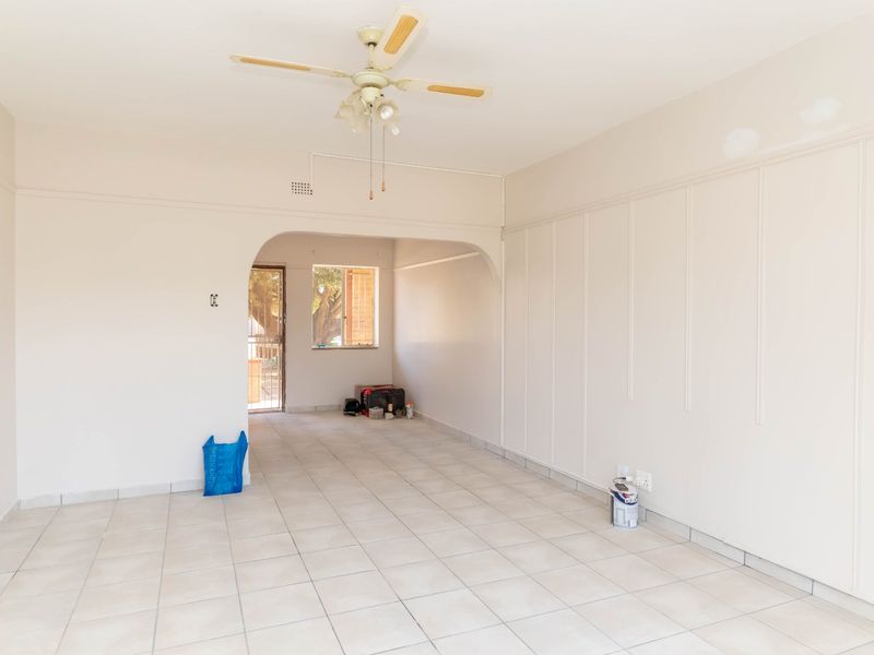 An empty living room featuring tiled flooring, a ceiling fan, and decorative wall paneling, currently undergoing minor wall repairs.