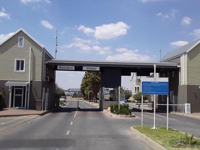 The main entrance to the residential complex featuring a secure gatehouse, boom gates for residents and visitors, and paved access roads.