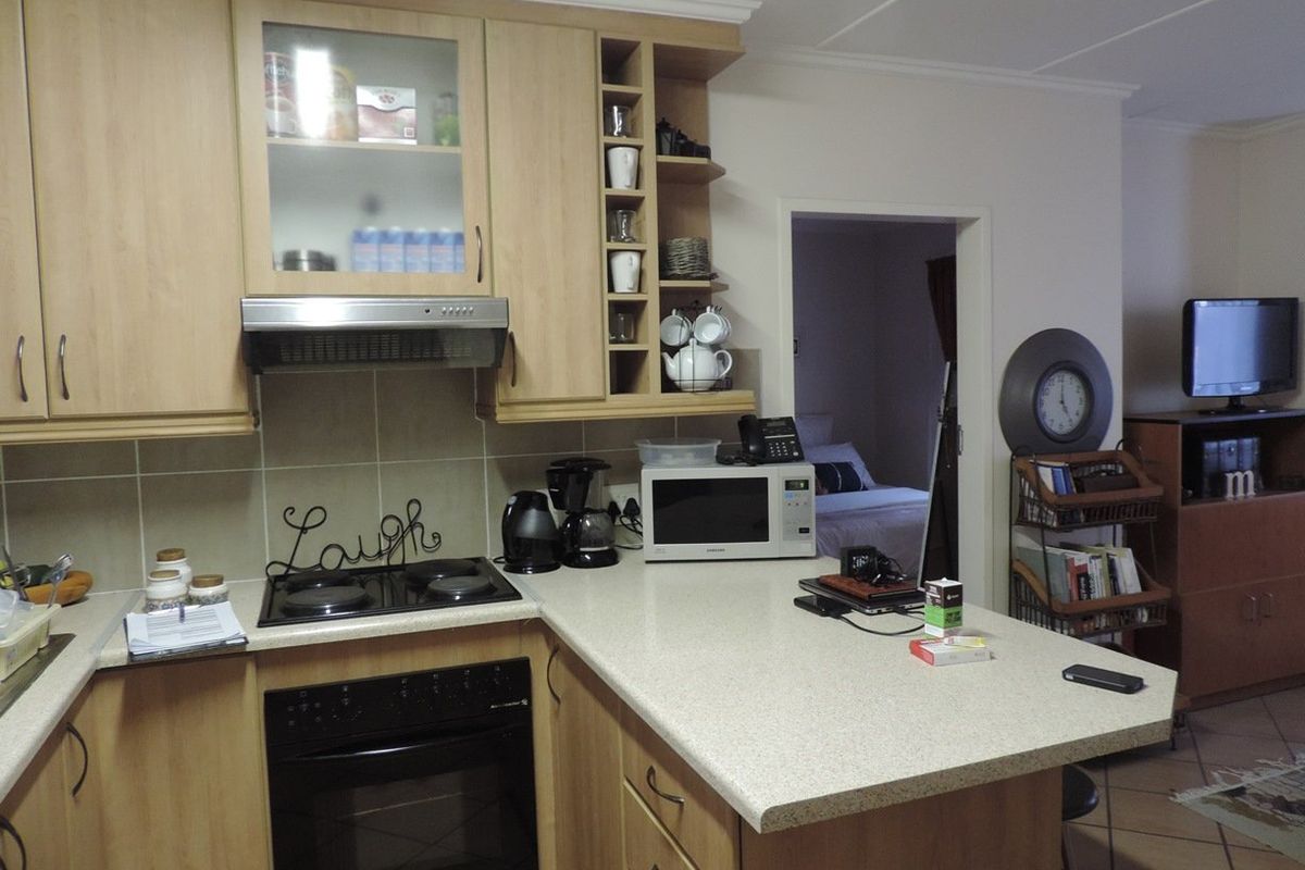 A functional kitchen featuring light wood-finish cabinetry, a built-in oven with electric hob, and a tiled backsplash, opening into an adjacent living area.