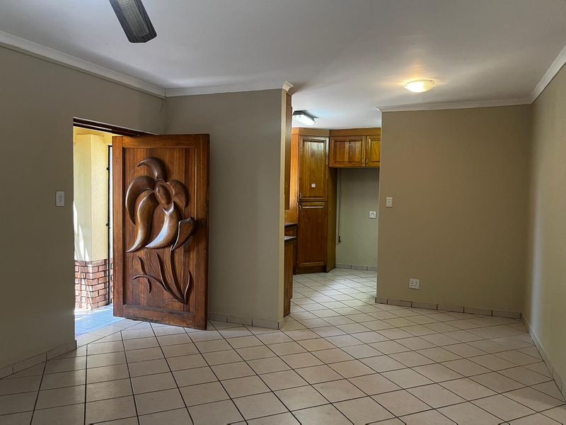 Open plan living area featuring tiled flooring, a decorative carved wooden entrance door, and a functional kitchen space with built-in wooden cabinetry.