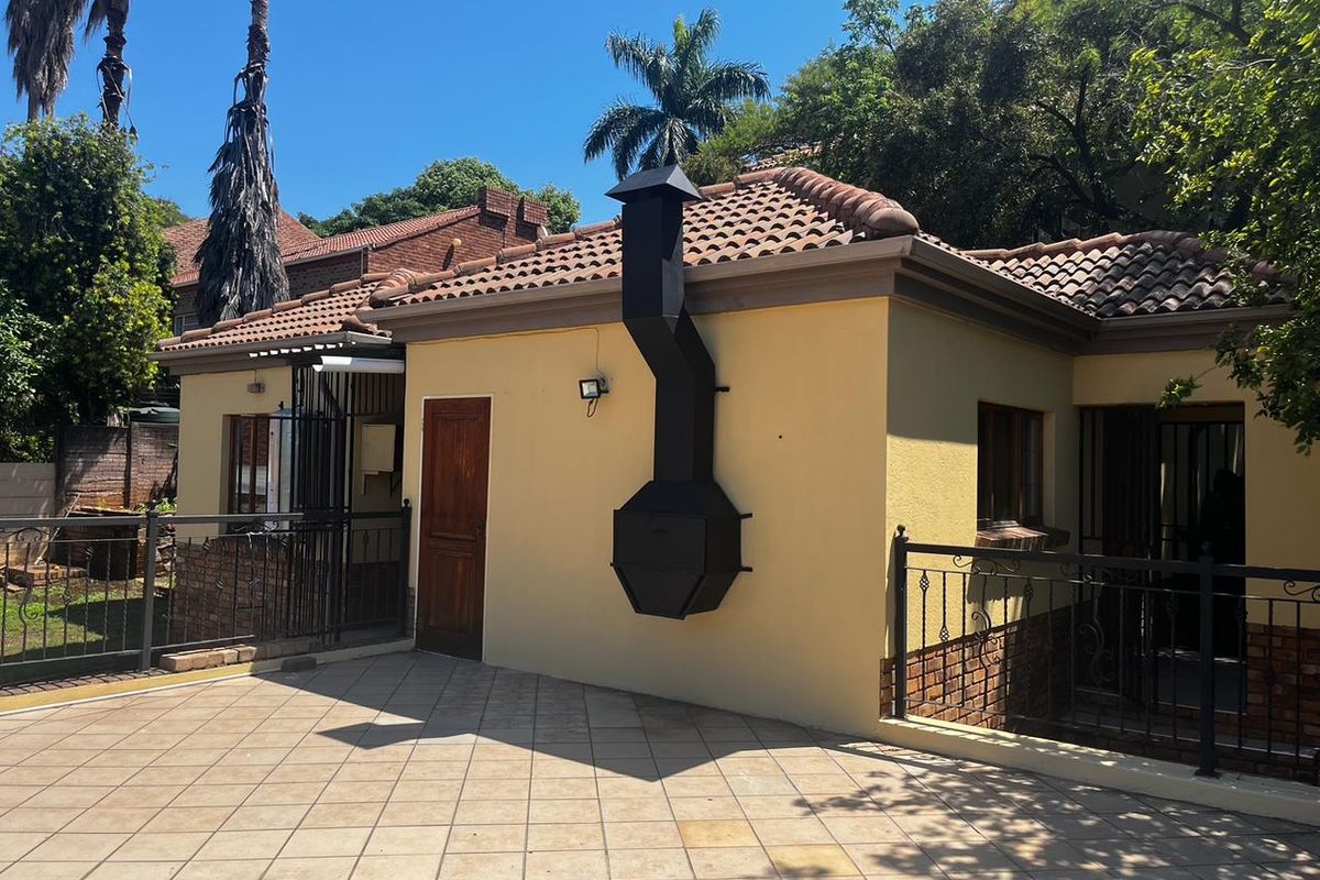 A well-maintained rear exterior area featuring a tiled patio, an external fireplace, and secure wrought iron fencing.