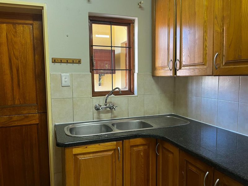 A functional scullery area featuring timber cabinetry, granite countertops, a double stainless steel sink, and a tiled backsplash.