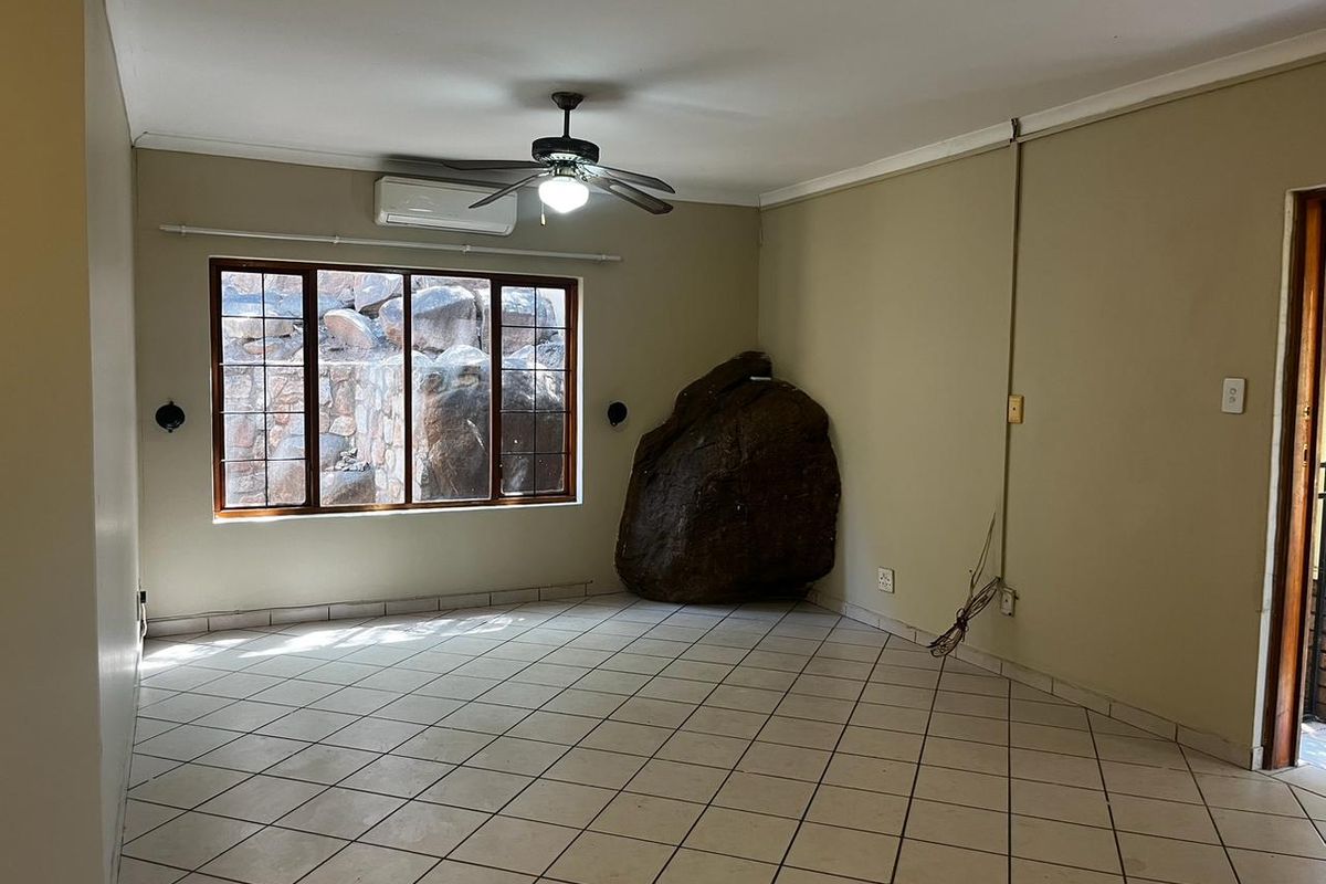 An empty living room featuring tiled floors, a ceiling fan, air conditioning, and a unique natural rock feature integrated into the interior space.