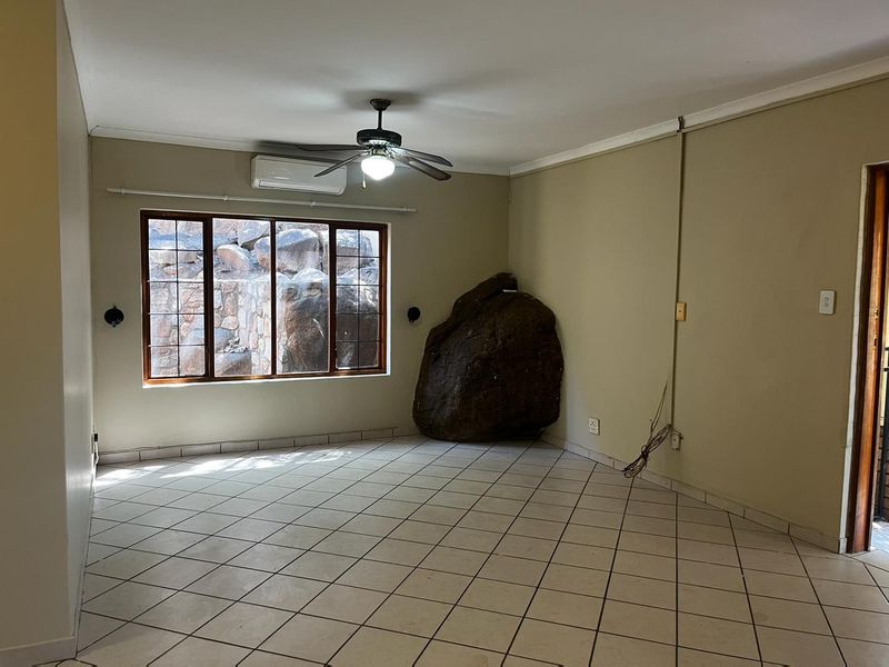 An empty living room featuring tiled floors, a ceiling fan, air conditioning, and a unique natural rock feature integrated into the interior space.