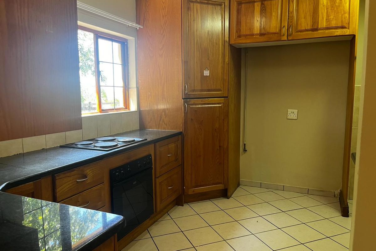 A functional kitchen featuring wooden cabinetry, granite countertops, an integrated oven and hob, and tiled flooring, offering a solid foundation for modern updates.