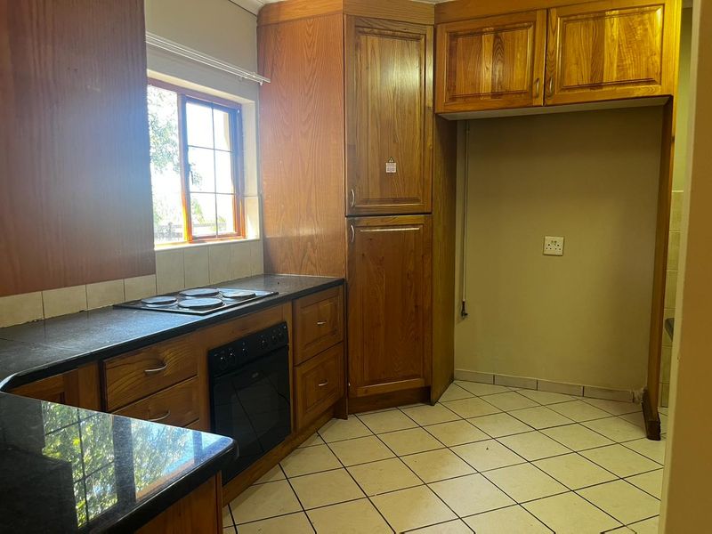 A functional kitchen featuring wooden cabinetry, granite countertops, an integrated oven and hob, and tiled flooring, offering a solid foundation for modern updates.