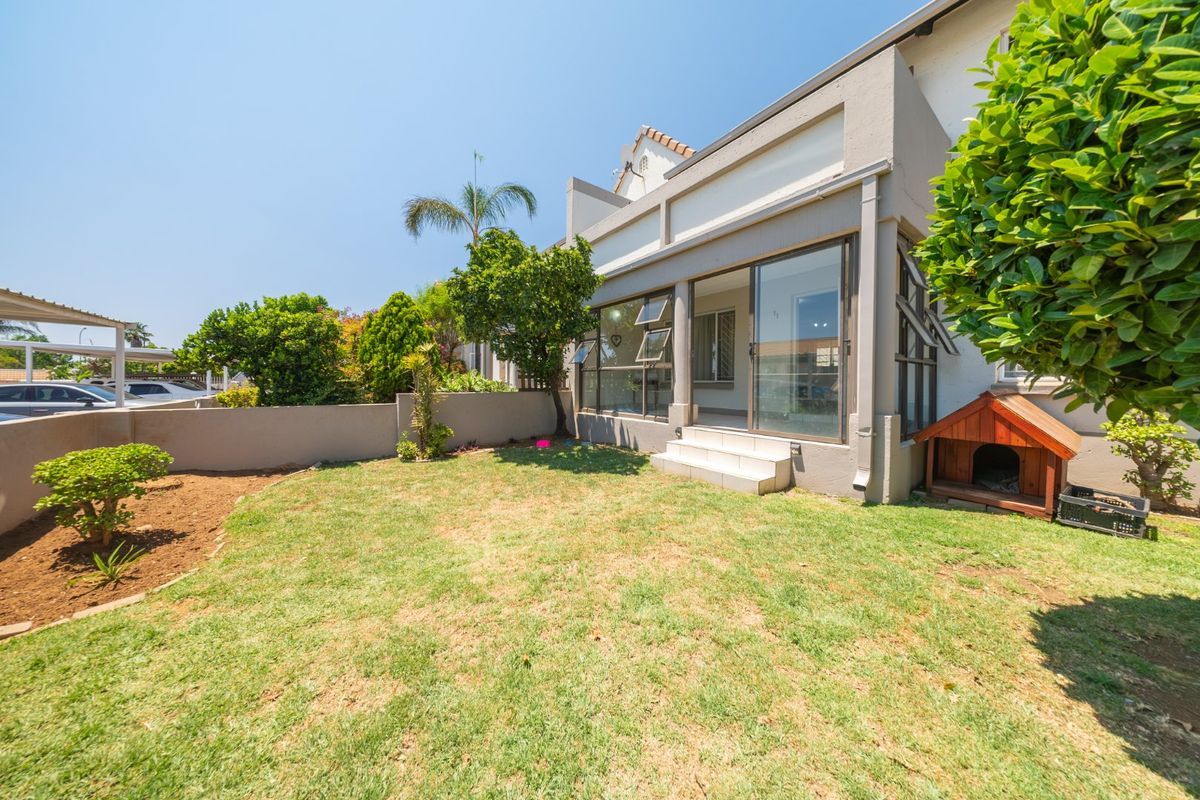 Rear view of the townhouse featuring a private garden, concrete boundary wall, and sliding glass doors leading to the interior living space.