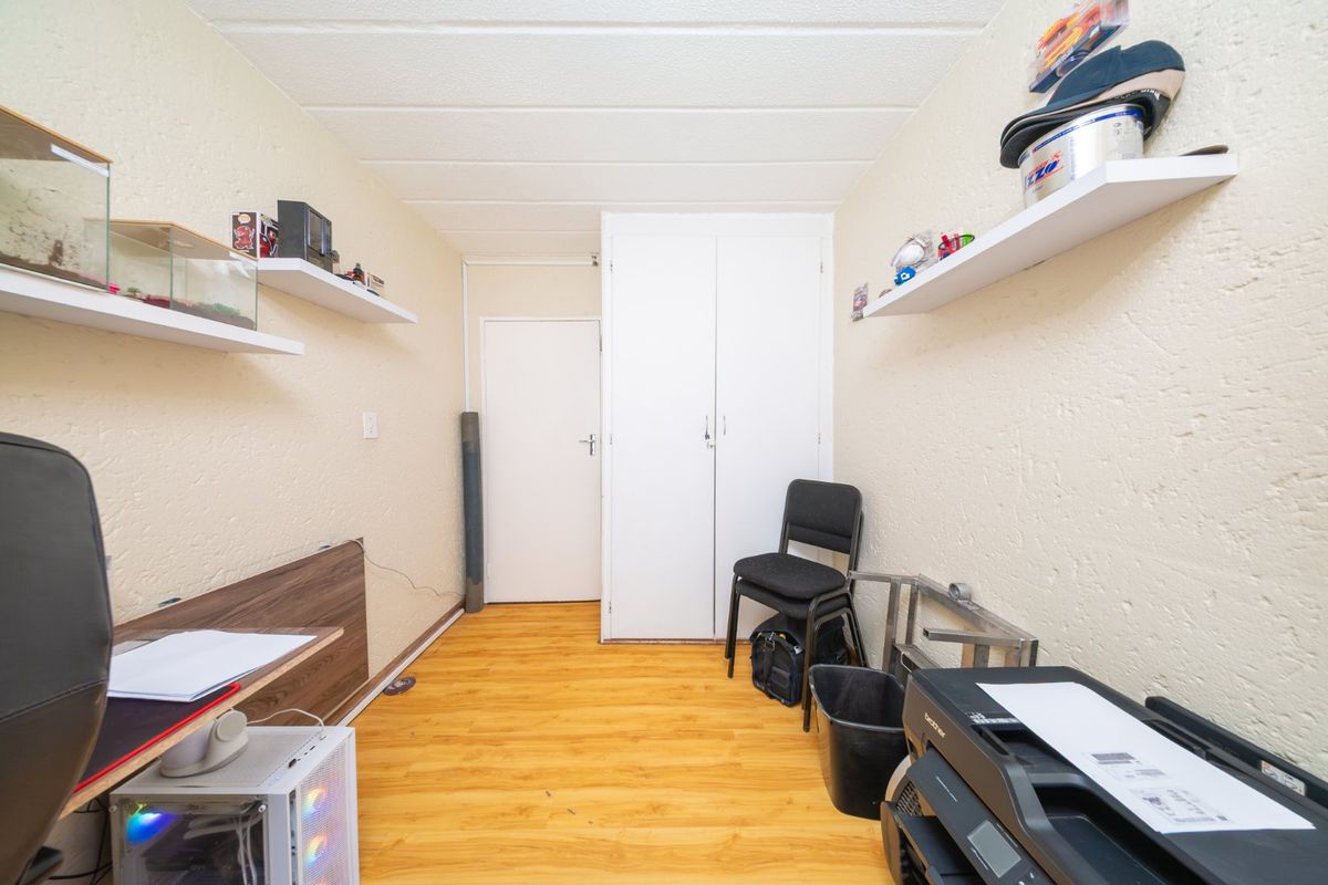A functional bedroom featuring laminate flooring, built-in wardrobe storage, and textured wall finishes, suitable for use as a bedroom or home office.