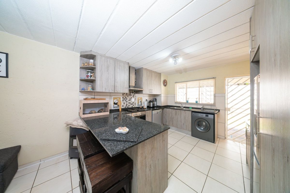 Functional kitchen featuring granite countertops, built-in cabinetry, integrated appliances, and tiled flooring with direct access to the exterior via a security gate.