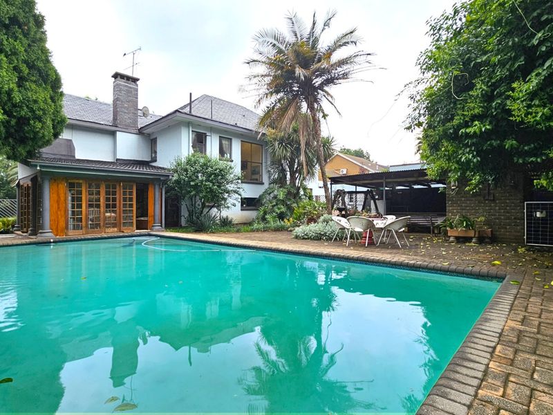 Spacious outdoor pool area featuring a large swimming pool, brick paved surround, and a covered patio area attached to the main residence.