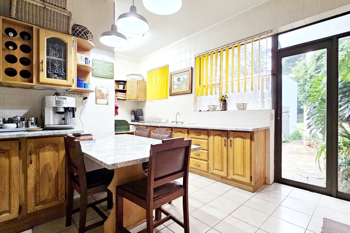 A functional kitchen featuring wooden cabinetry, tiled flooring, and a breakfast nook, with direct access to the outdoor area through a glass door.