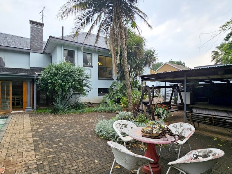 Rear exterior view featuring a paved patio area, swimming pool, and a covered outdoor space adjacent to the main house structure.