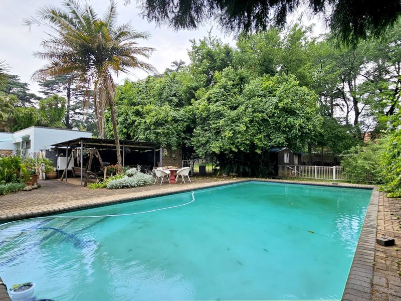 Outdoor pool area featuring a swimming pool, brick paved surround, and a covered patio space set within a mature garden.