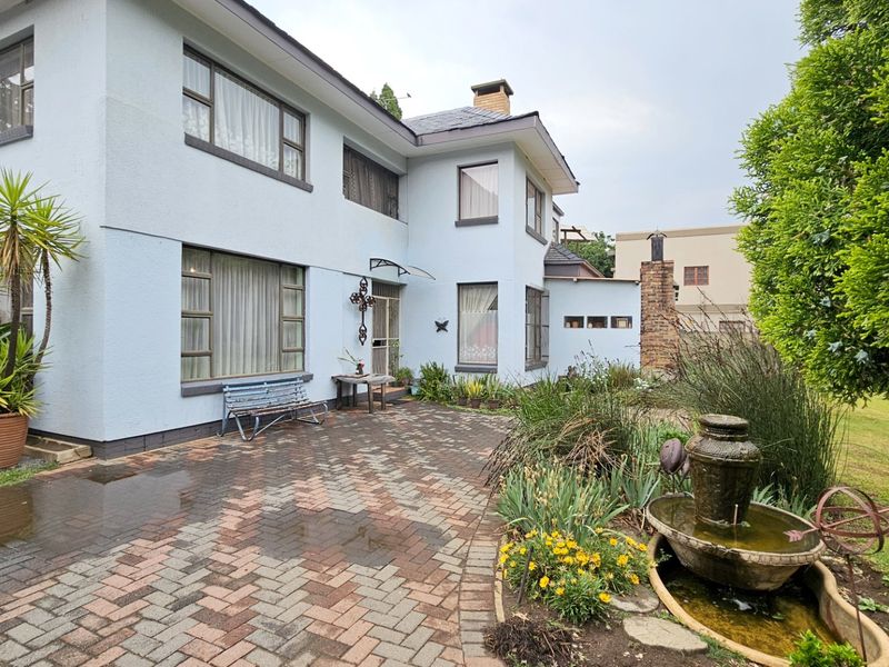 Rear exterior view of a two-story house featuring a brick-paved patio, a stone water feature, and established garden landscaping.