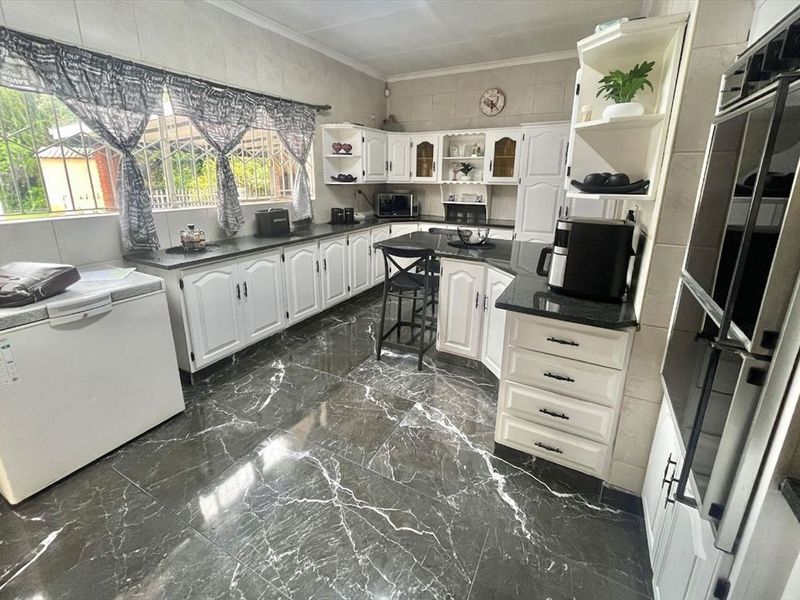 A spacious kitchen featuring white cabinetry, dark granite countertops, dark marble-style floor tiles, and a built-in double wall oven.