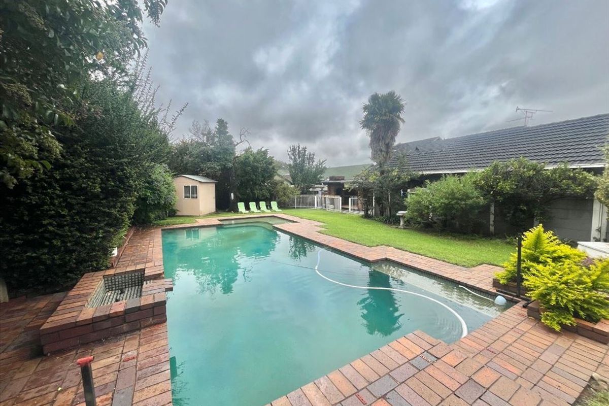A backyard area featuring a swimming pool with brick paving, a small garden shed, and established lawn and garden beds.