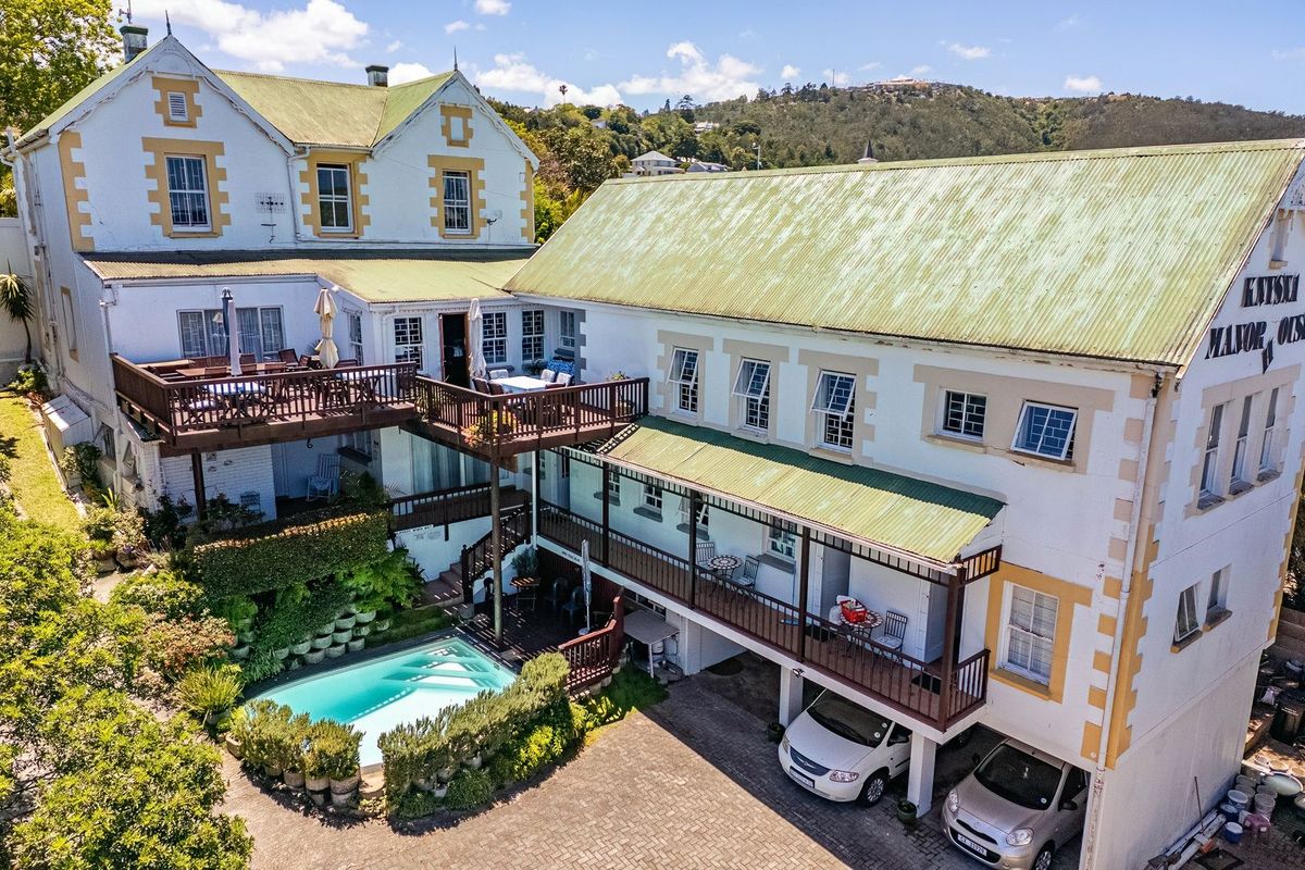 Aerial view of a multi-level commercial property featuring a swimming pool, timber decking, covered parking, and traditional architectural styling.