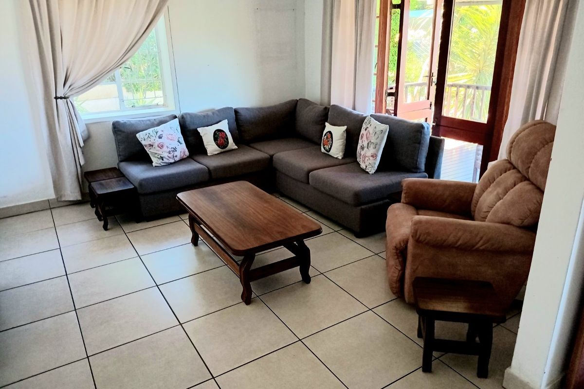 A bright living room featuring neutral tiled flooring and direct access to an outdoor area through double glass doors.