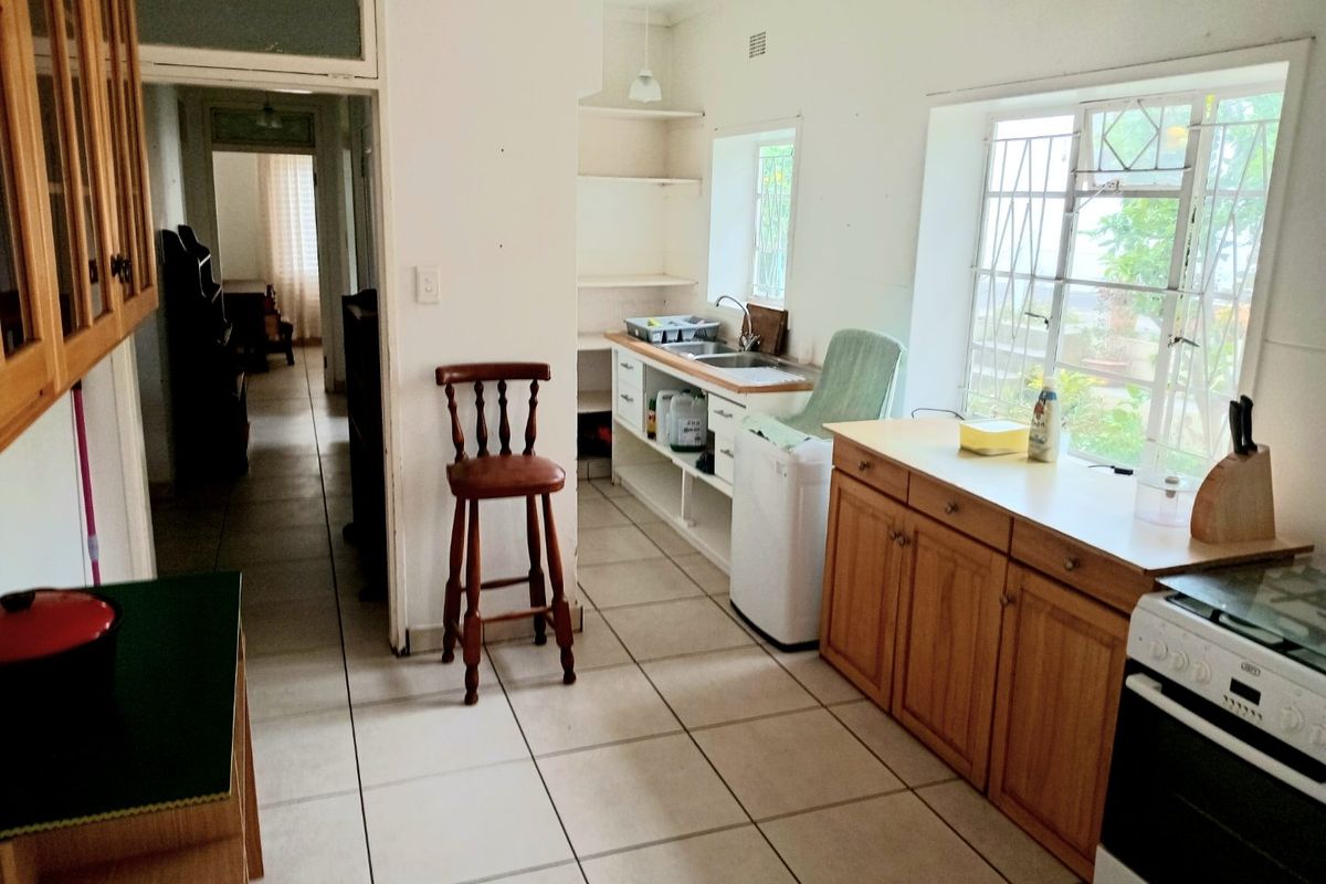 A functional kitchen featuring tiled flooring, wooden cabinetry, a double sink, and a freestanding stove, with direct access to the hallway.