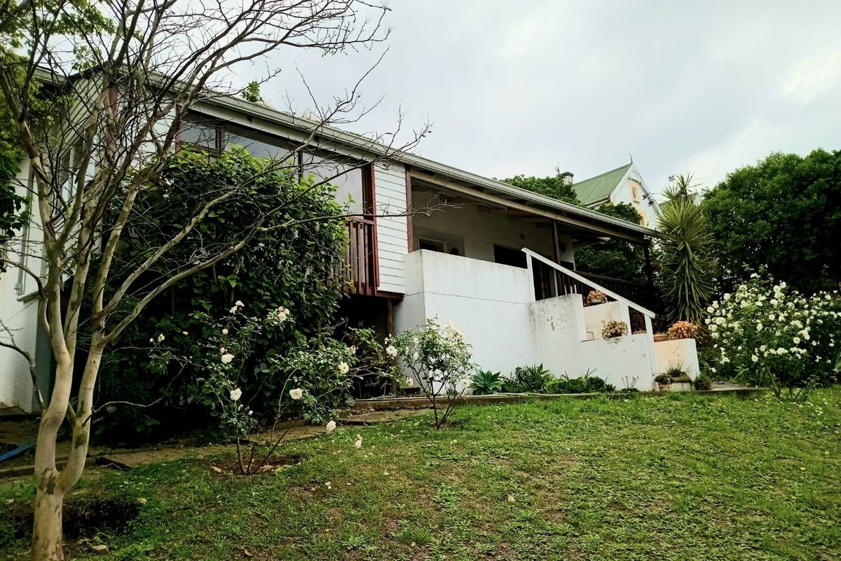 Rear view of the property featuring a raised timber deck, weatherboard cladding, and access stairs leading to a garden area.