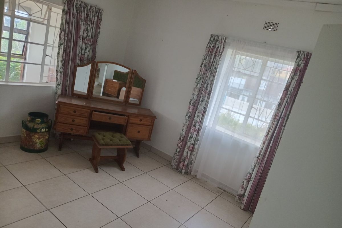 A bedroom featuring tiled flooring, a ceiling fan, and windows fitted with security bars, offering a functional and well-lit space.