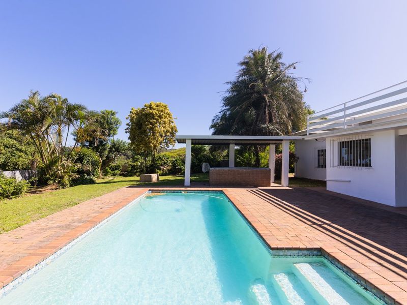Outdoor pool area featuring a rectangular swimming pool, brick paved surround, and a covered patio with a built-in braai area.