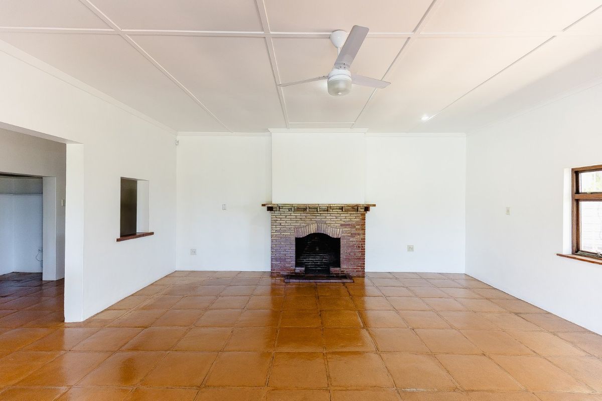 Spacious living room featuring a classic brick fireplace, tiled flooring, and a ceiling fan, offering a clean and versatile blank canvas.
