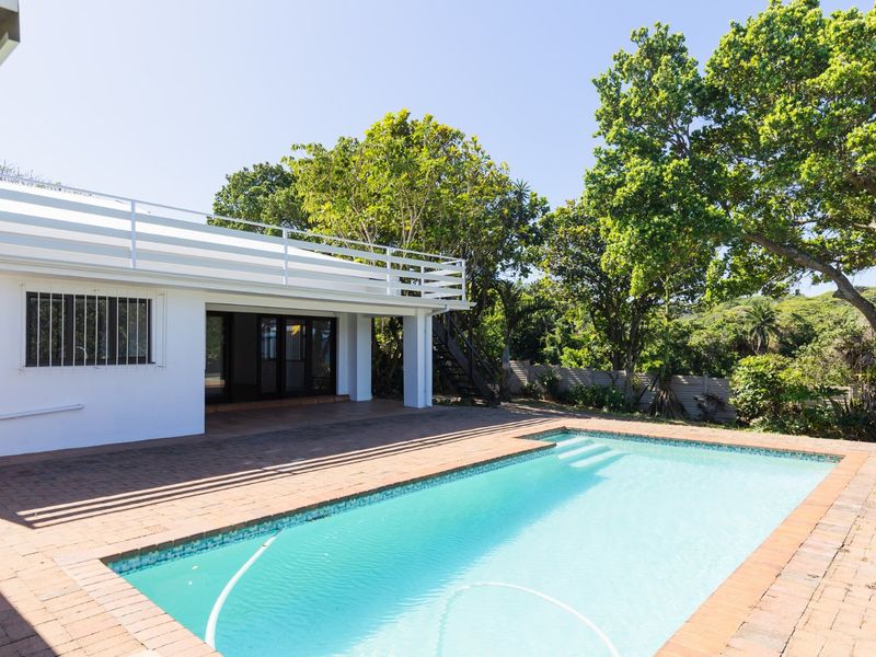 Outdoor pool area featuring brick paving, a swimming pool, and a balcony with an external staircase leading to the upper level.