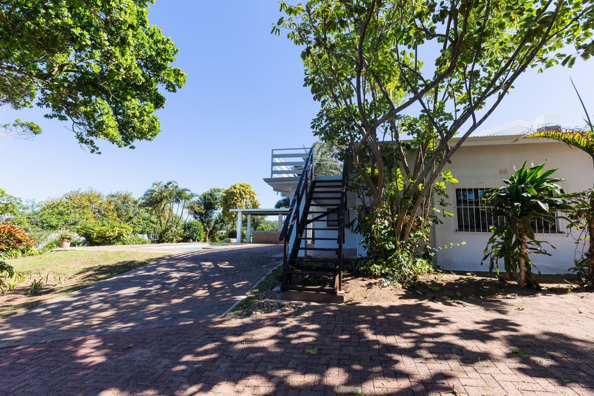 Rear exterior view featuring a paved area, external staircase leading to a balcony, and a swimming pool set within a landscaped garden.