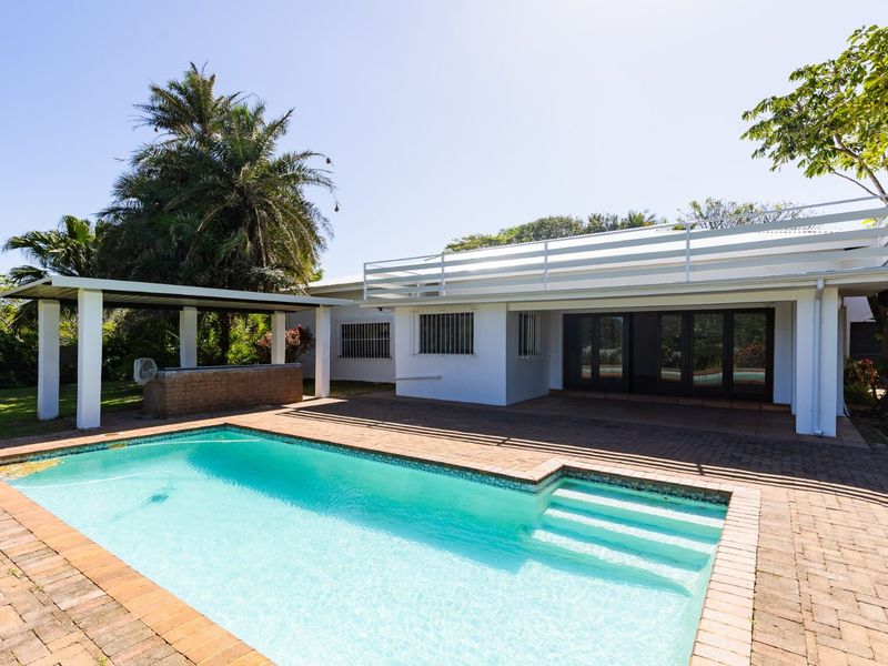 Outdoor pool area featuring a swimming pool, brick paved surround, and a covered patio with a built-in bar counter.