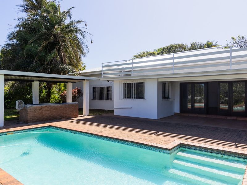 Outdoor pool area featuring a brick-paved patio, a covered bar structure, and direct access to the home through sliding glass doors.