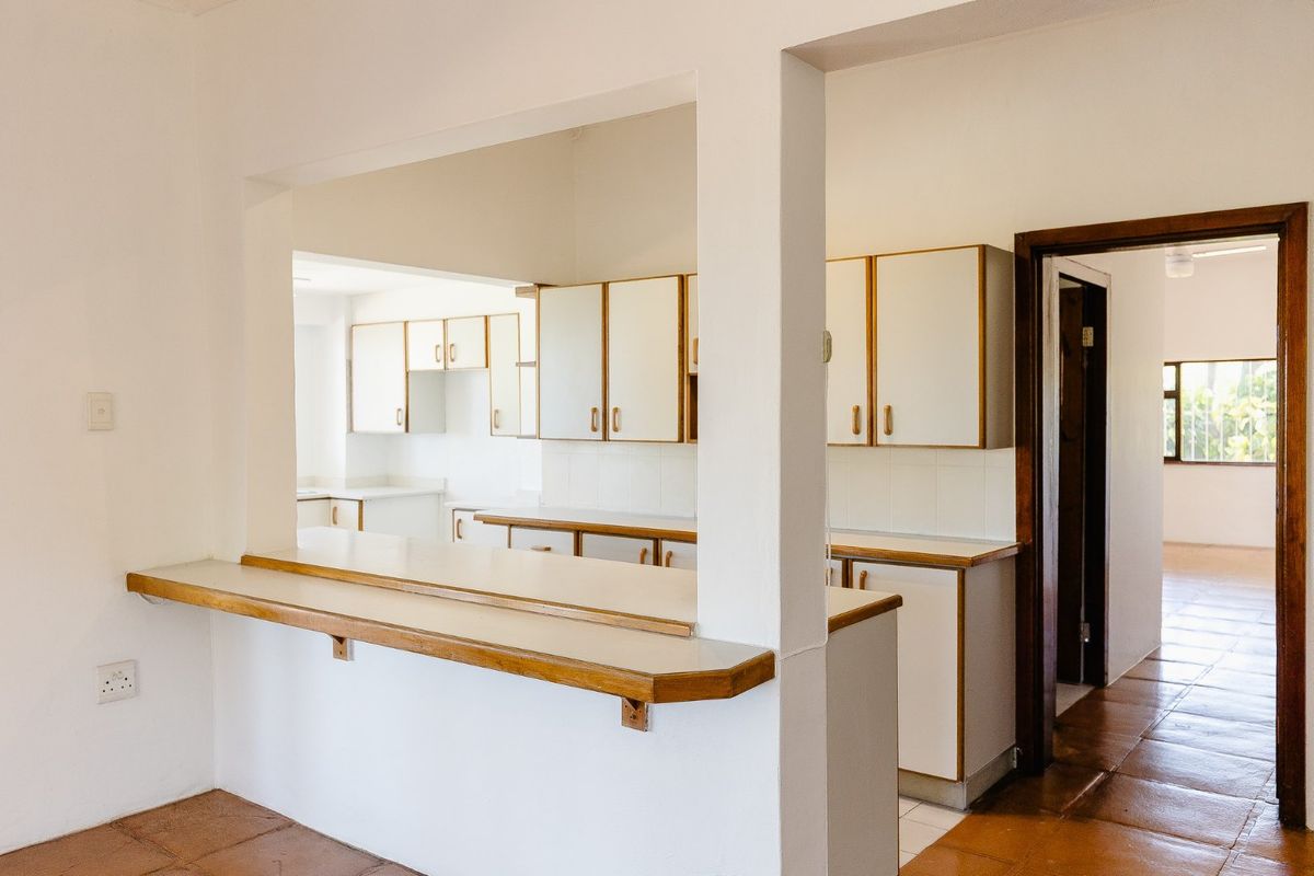 A functional, empty kitchen featuring white cabinetry, a breakfast bar, and tiled flooring, offering a clean canvas for potential updates or modern styling.