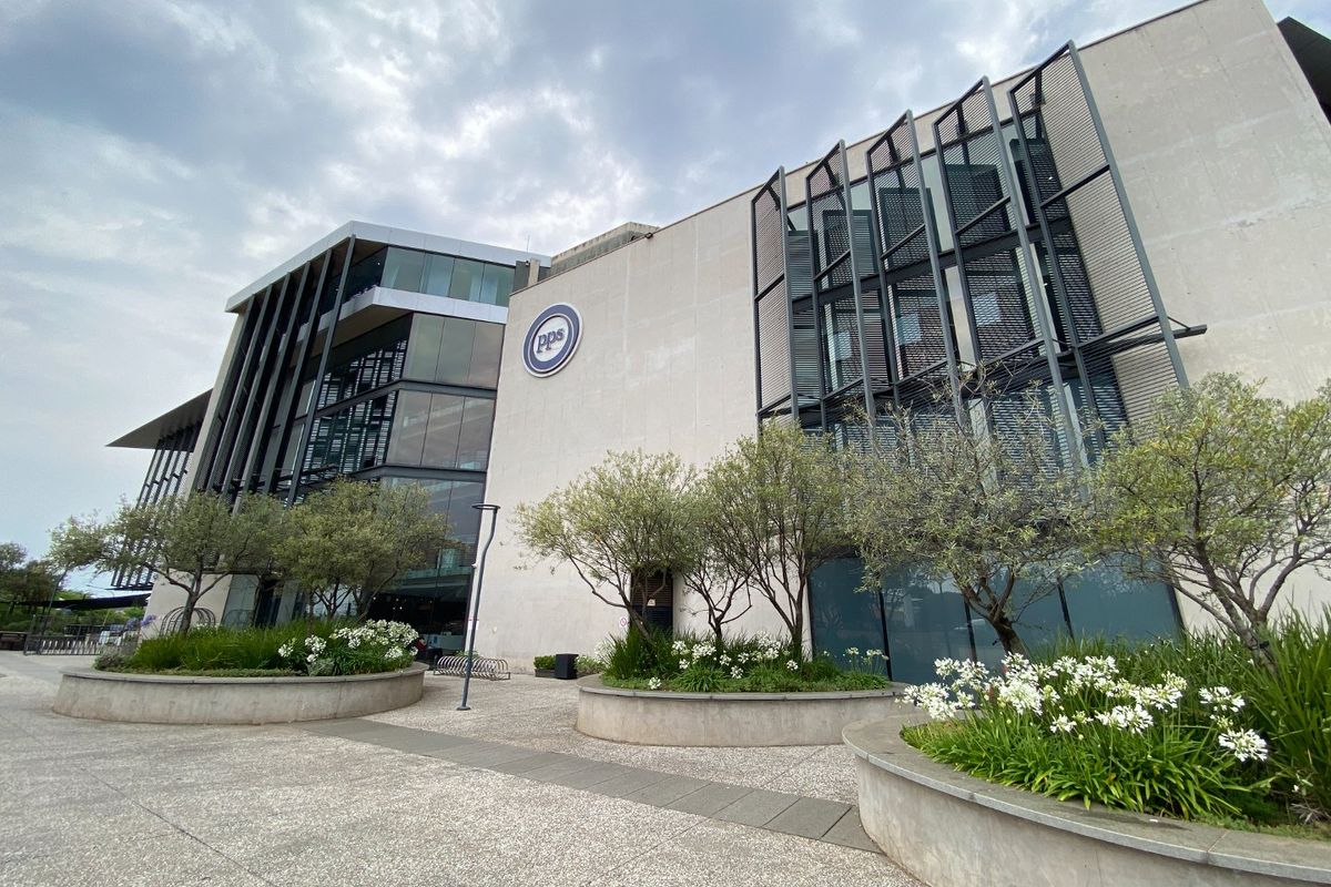 Modern commercial office building facade featuring glass curtain walls, metal louvers, and landscaped concrete planters in the foreground.