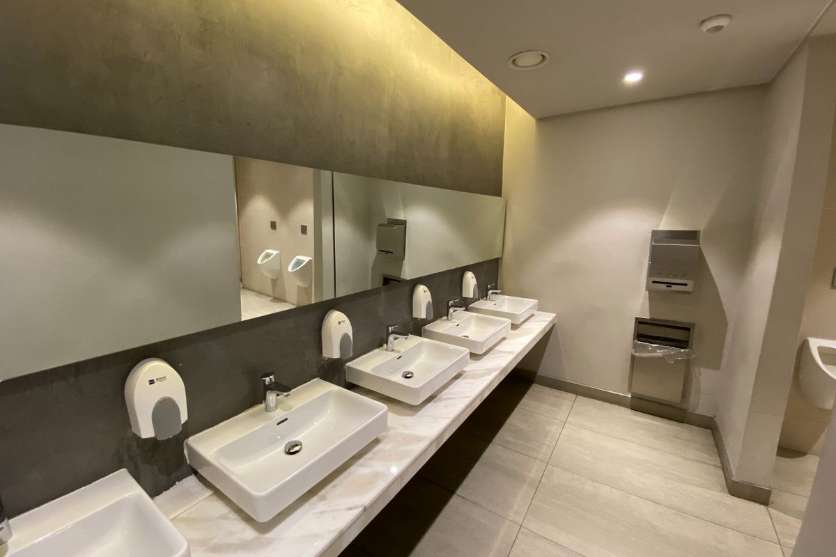 Modern commercial restroom featuring a long marble vanity with multiple vessel sinks, large wall-to-wall mirrors, and recessed ceiling lighting.