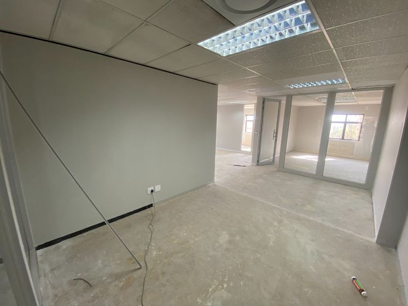 An empty commercial office space featuring glass partitions, suspended ceilings with recessed lighting, and unfinished concrete flooring, ready for tenant fit-out.