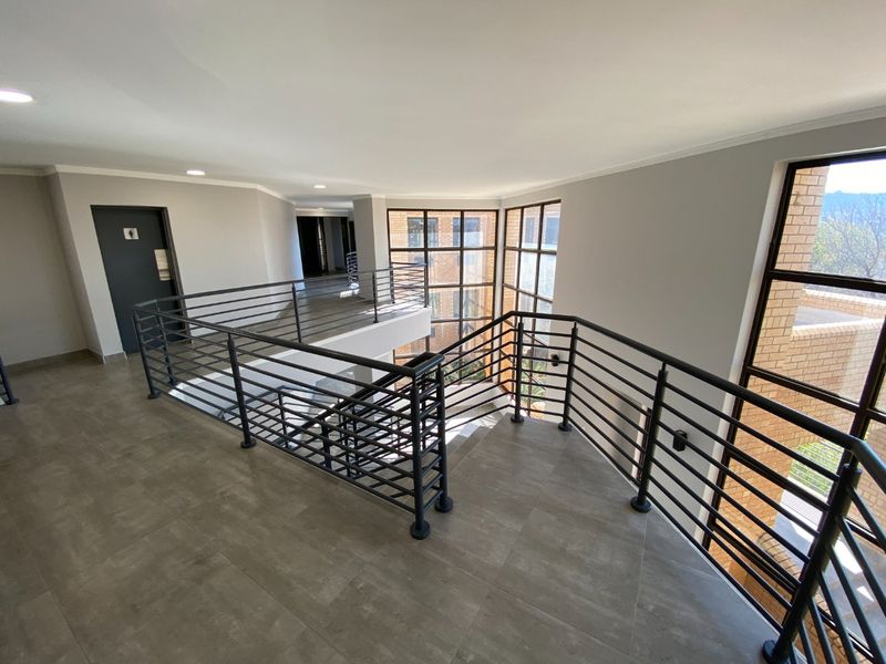 A modern, spacious commercial hallway featuring tiled flooring, a sleek metal balustrade overlooking the staircase, and large windows providing ample natural light.