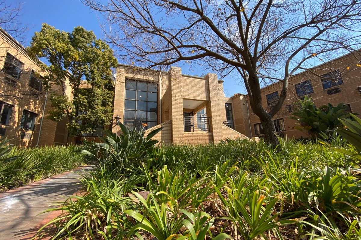 A view of the commercial building's front facade featuring brick construction, large windows, and a landscaped garden entrance.