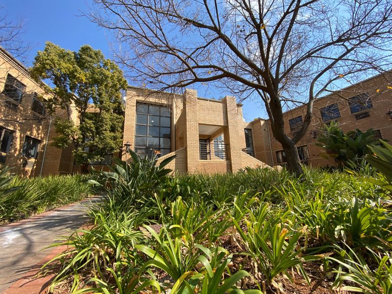 A view of the commercial building's front facade featuring brick construction, large windows, and a landscaped garden entrance.
